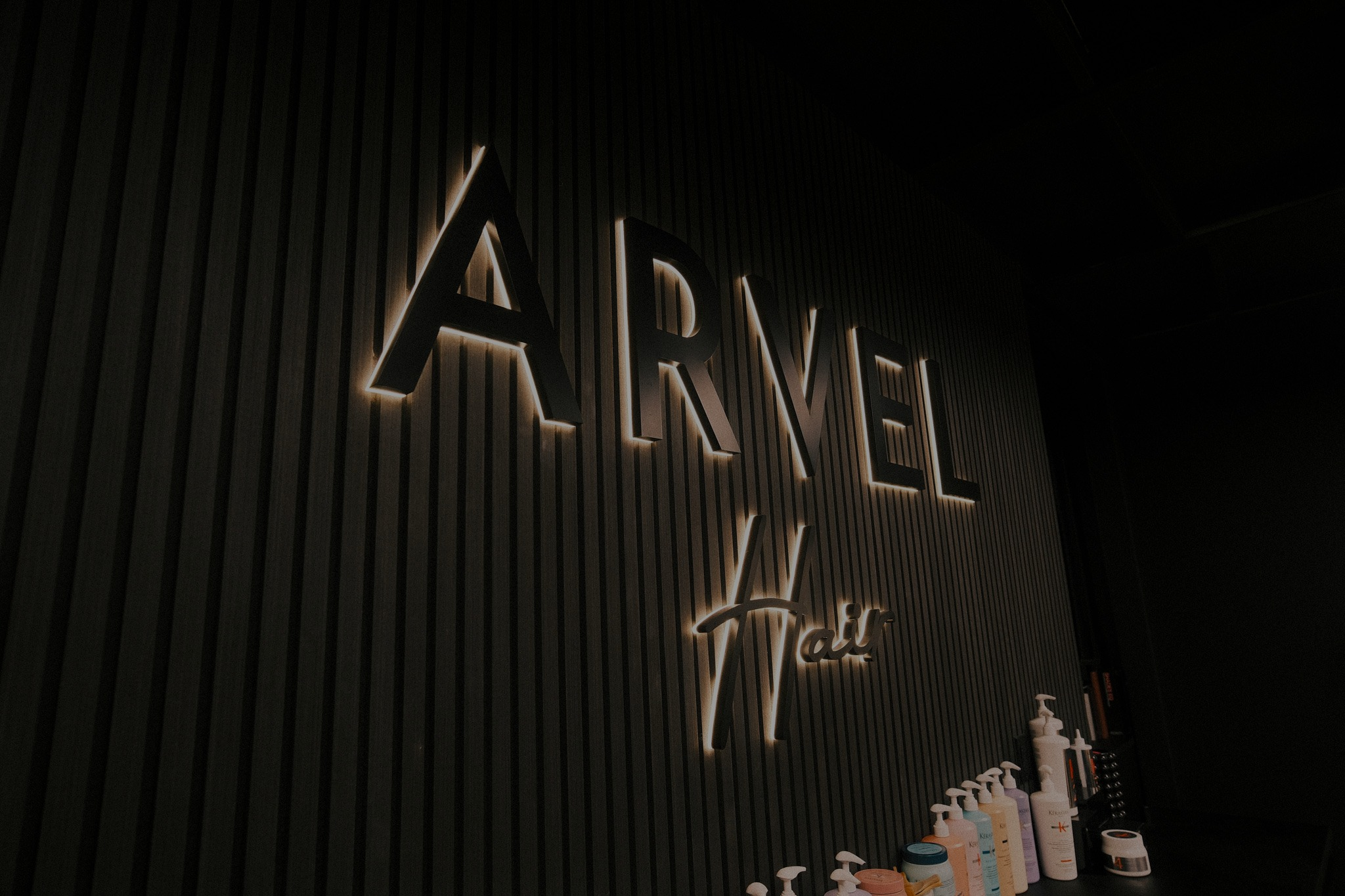 Illuminated Arvel Hair logo sign on black slat wall